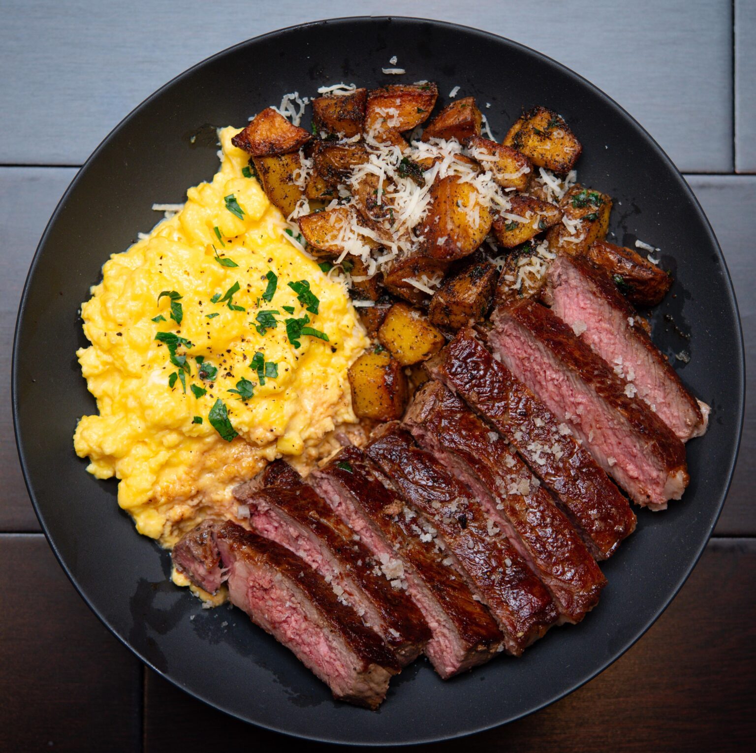[homemade] ribeye steak, scrambled eggs with crème fraiche and garlic Parmesan potatoes fried in butter.