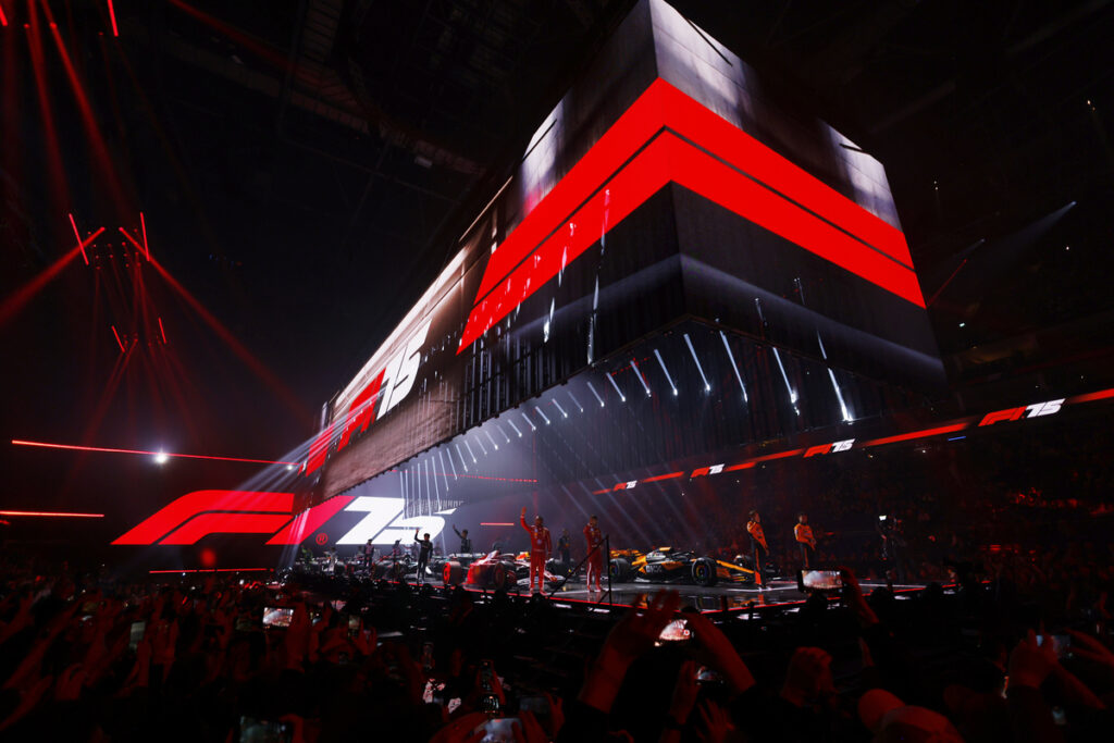 Formula 1 75th anniversary celebration event with F1 cars and drivers on stage, surrounded by red lights and a crowd