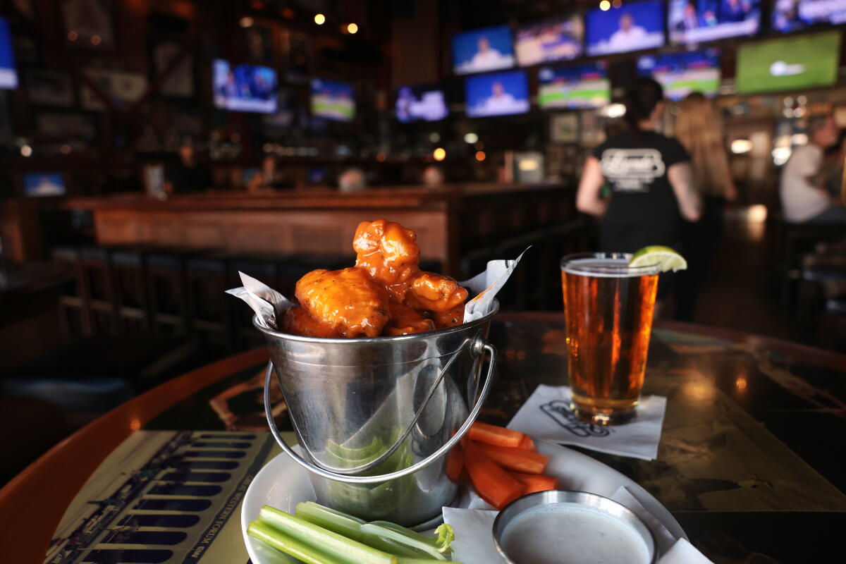 An order of buffalo wings and a pint of beer resting on a table; in background, a bank of TVs tuned to sports programming