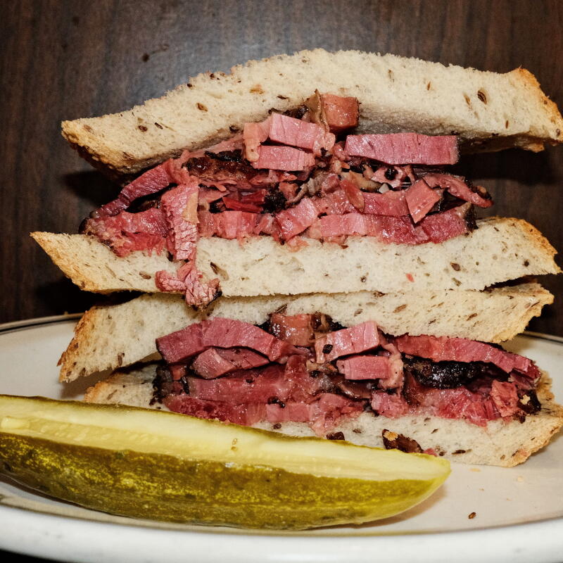 Two stacked halves of a plain hot pastrami sandwich on rye at Langer's Delicatessen-Restaurant in Westlake. Pickle on plate.