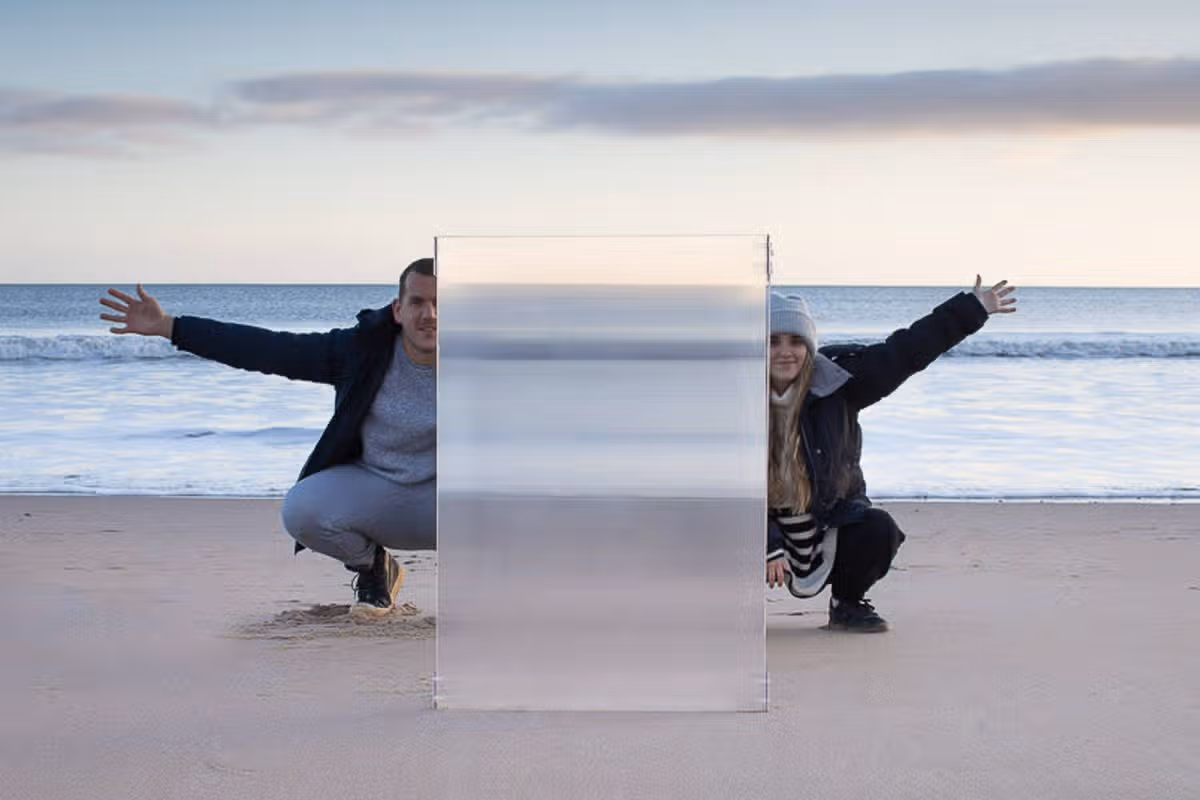 An individual is depicted in a dynamic pose on a sandy beach, with arms extended and legs spread, under a clear sky. The scene includes a split-screen effect, showcasing a mirrored version of the same individual. The setting is tranquil with a serene ocean in the background.