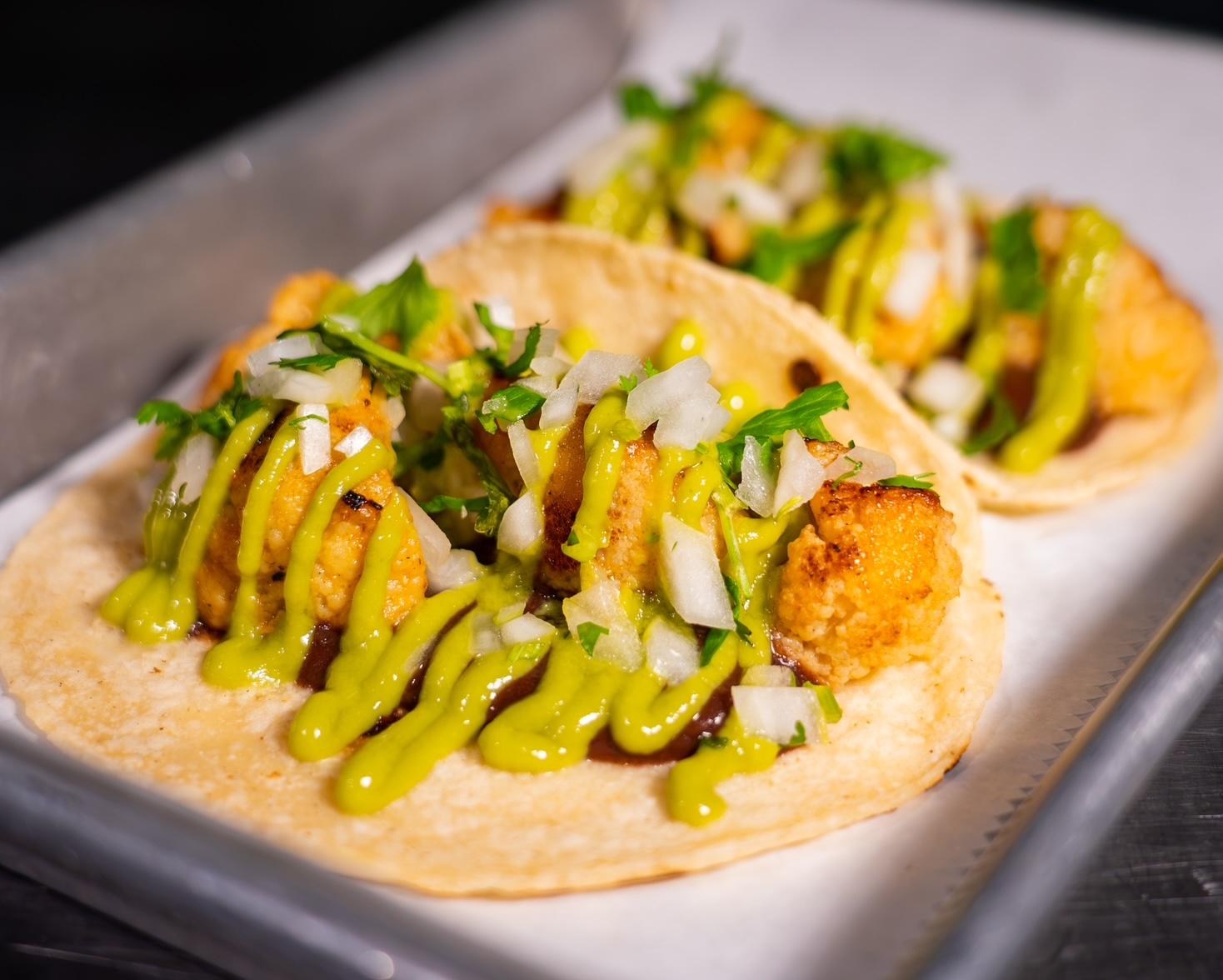 Two cauliflower tacos drizzeled in a rich, bright green salsa.