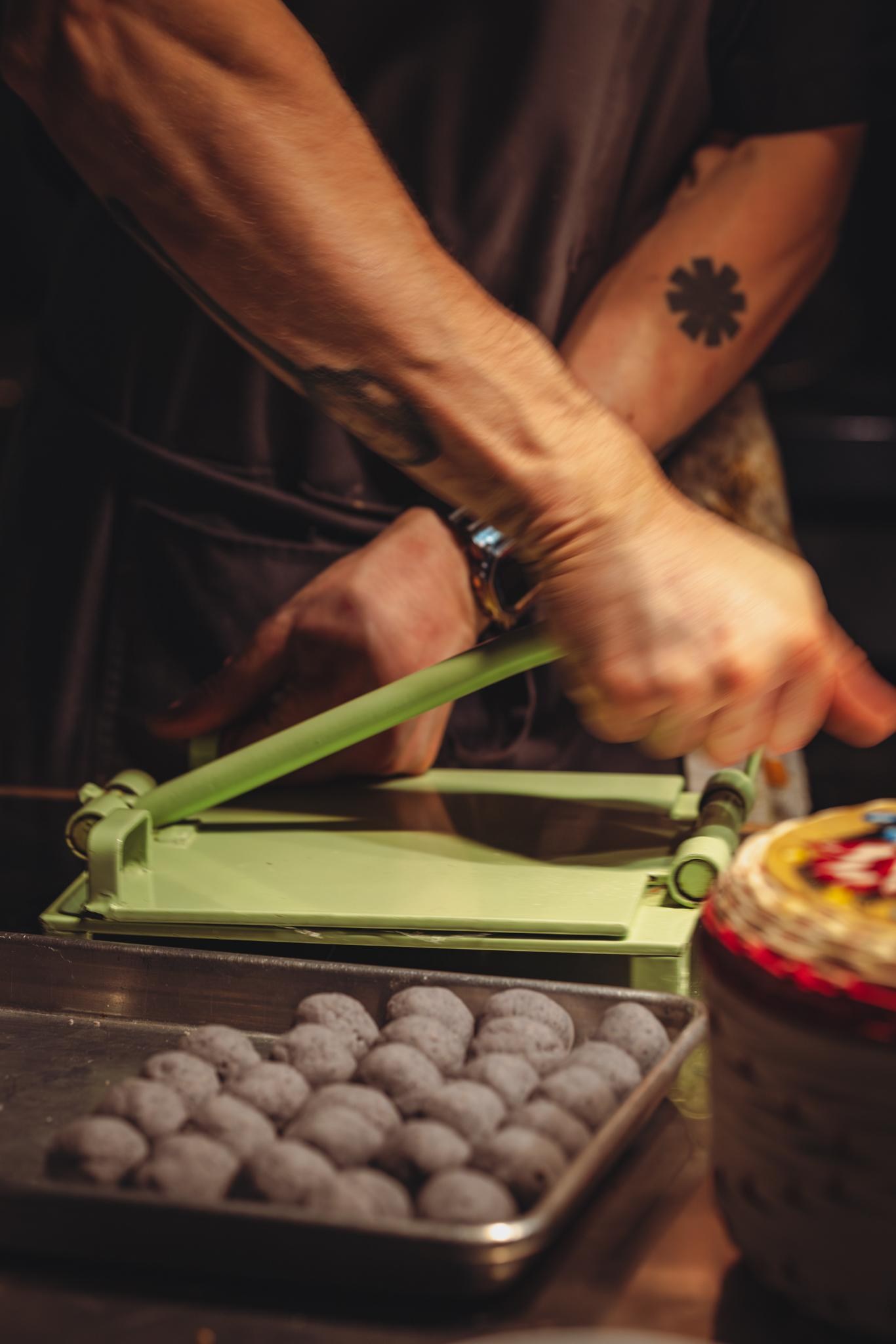 Hands use a tortilla press next to balls of blue corn masa.