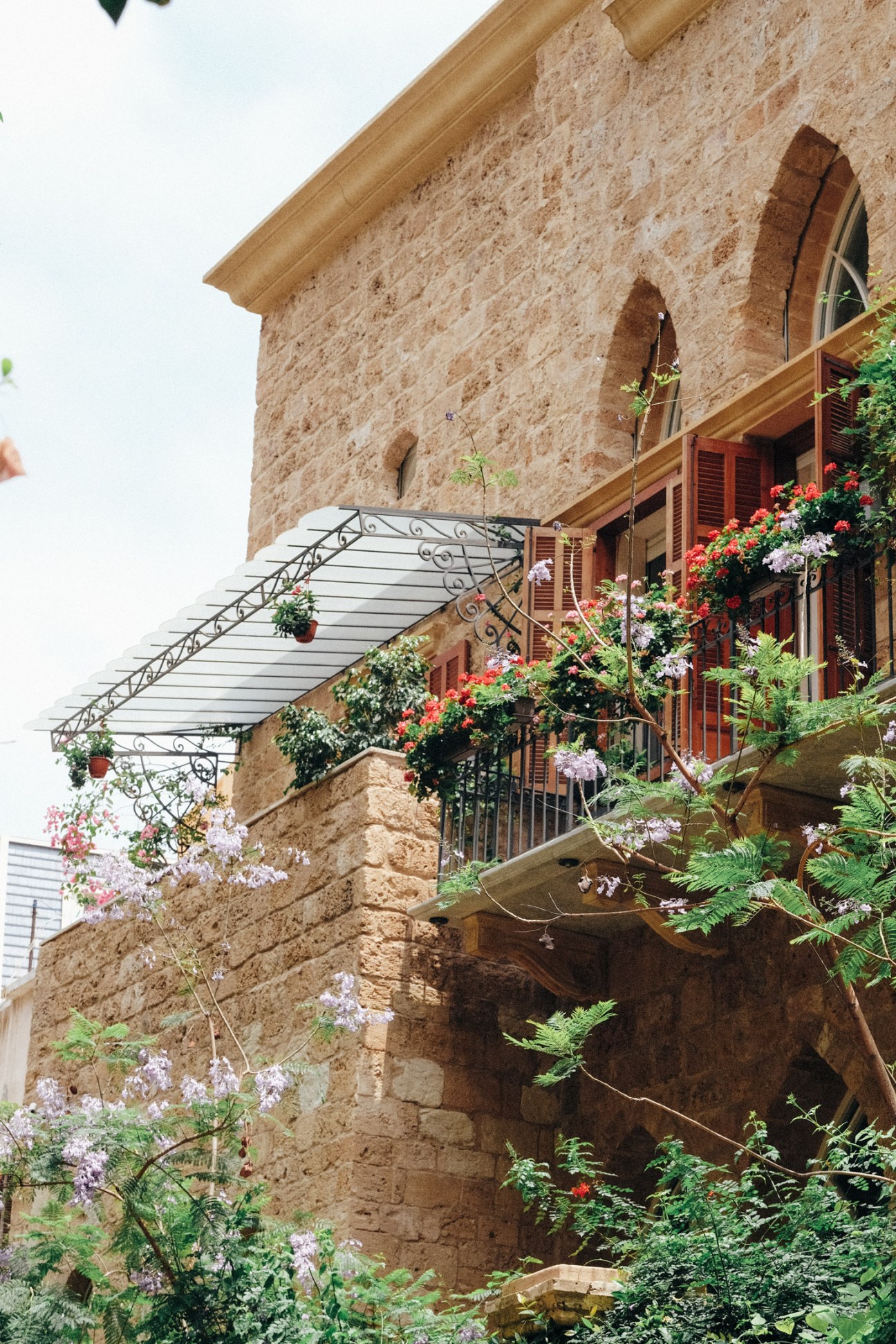 Ottoman-era stone building with wooden shutters and flowering plants cascading from multiple balconies.