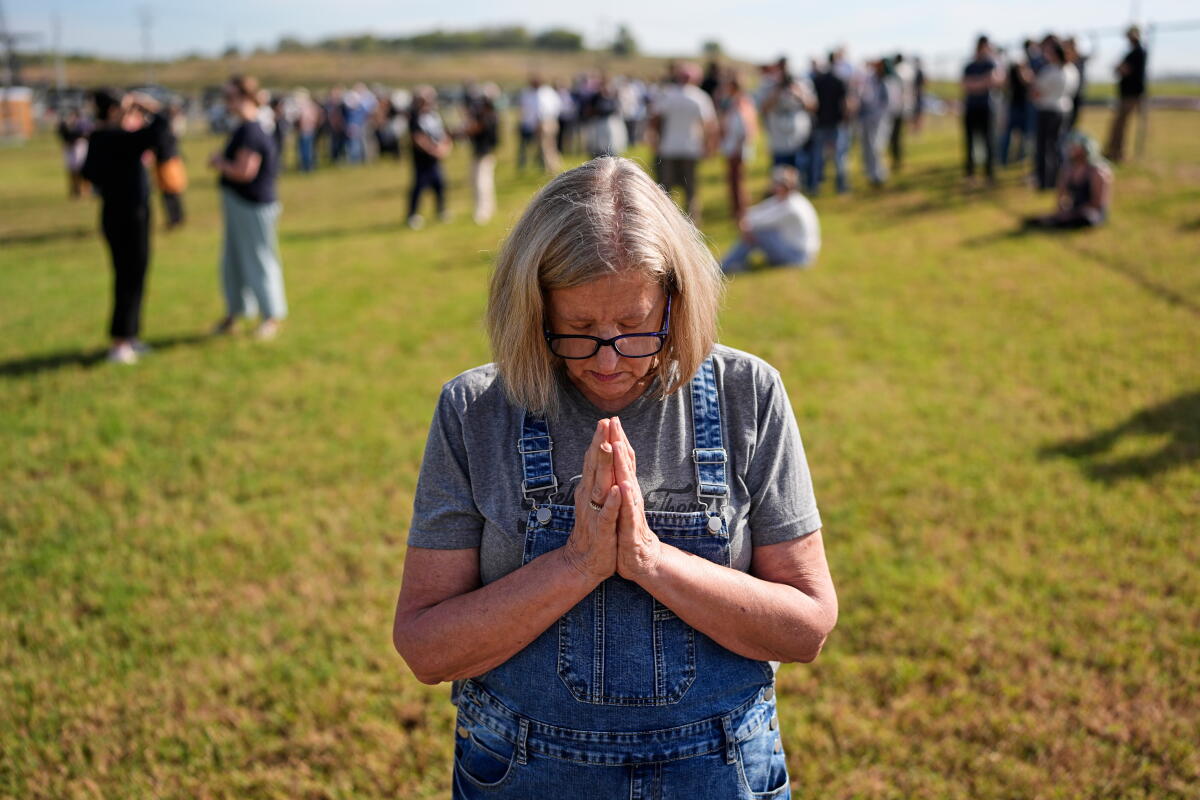 A woman prays outside on grass, with others in the background at a slight distance 