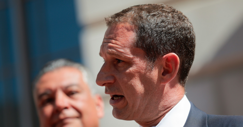 Lurie declares rent emergency as SF housing costs surge A man in a suit and blue tie speaks into multiple microphones, while another man in the background listens attentively.
