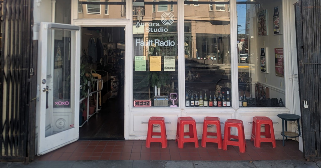 Valencia’s Studio Aurora is saying goodbye with a pinsa party and huge wine sale A storefront with glass windows and an open door displays "Aurora Studio" and "Fault Radio," with five red stools outside and various bottles lined up in the window.