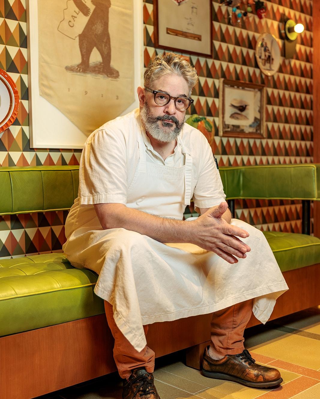 Jeremy Fox at Birdie G’s in a white apron sitting on a green couch.