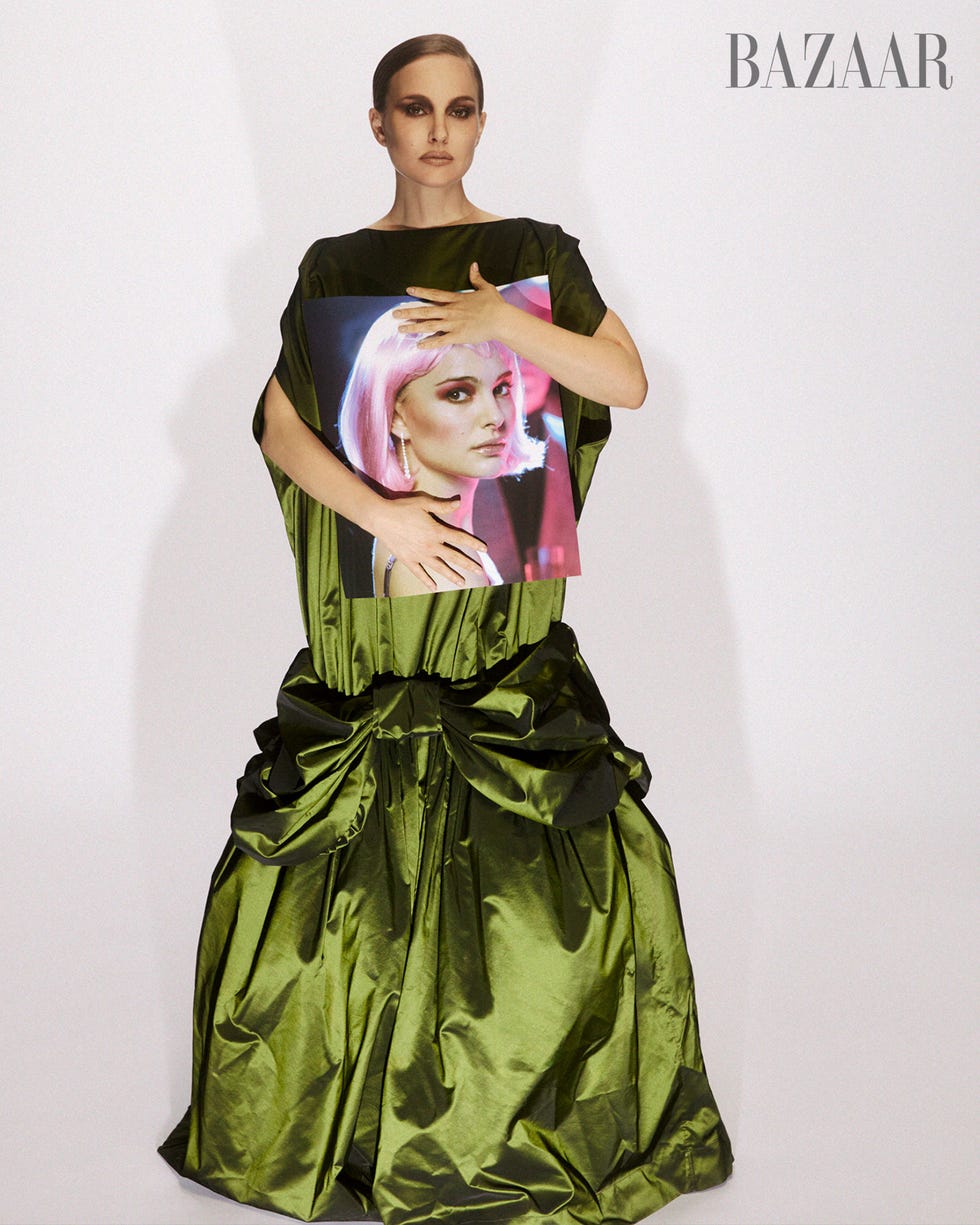 Model wearing a dramatic green gown, holding a portrait of a woman with pink hair, with a minimalist background. Model wearing a dramatic green gown, holding a portrait of a woman with pink hair, with a minimalist background.