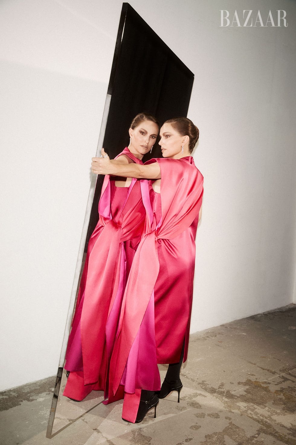 A model in a pink gown poses with a mirror, reflecting her image in an artistic fashion shoot. A model in a pink gown poses with a mirror, reflecting her image in an artistic fashion shoot.