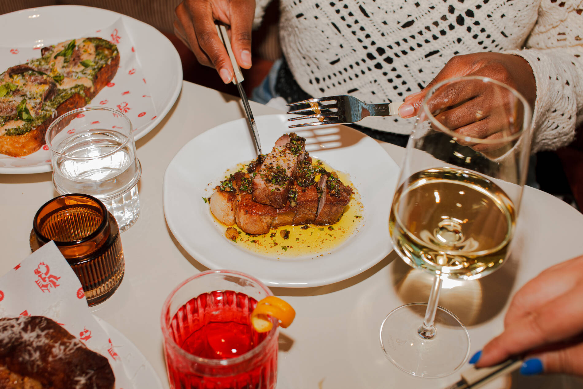 A person cutting into a gourmet dish on a table with drinks.