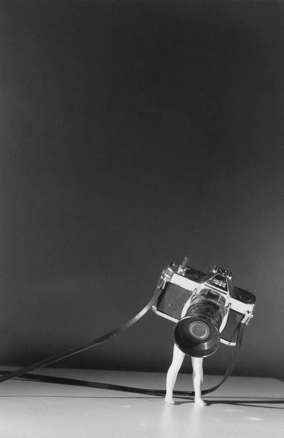 Miniature figure with a vintage camera lens on black background, creating an artistic and surreal scene.