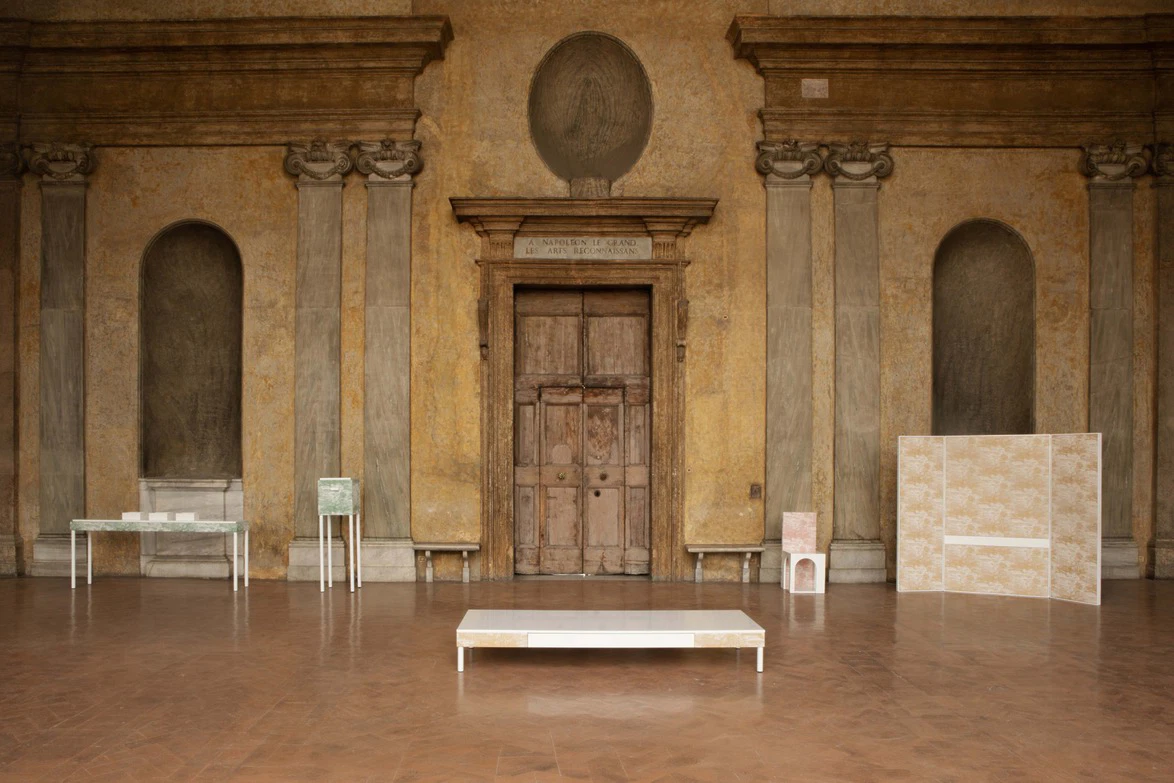 Historic architecture with wooden door, tall columns, and three minimalist art displays in a spacious gallery setting.
